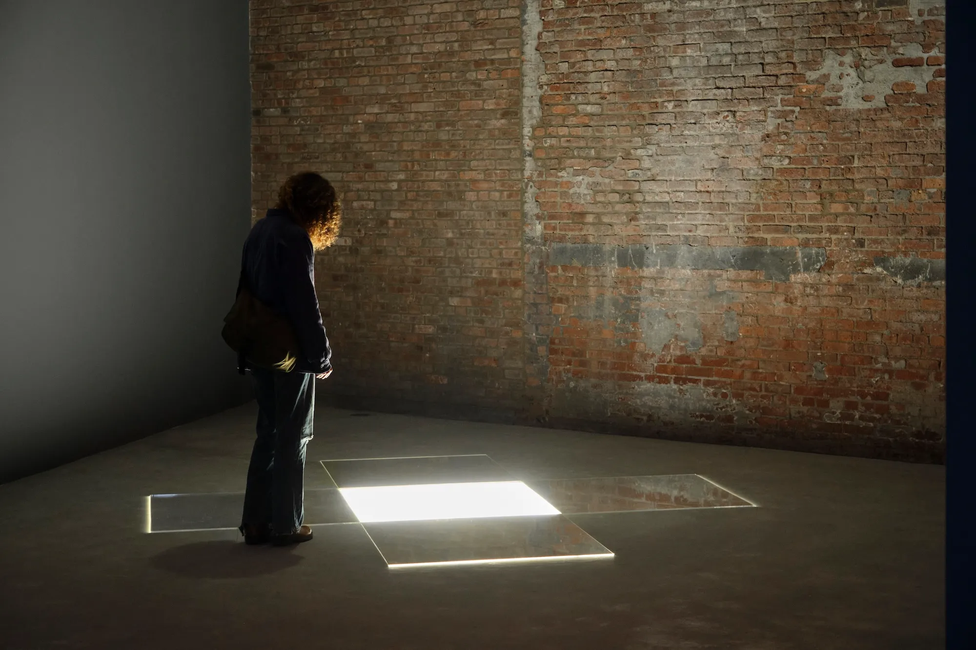 Visitor standing over glowing square floor panels in dim brick-walled space.
