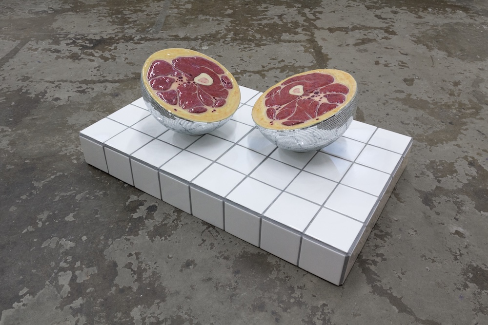 Two flesh-like sculptural halves displayed on a white tiled pedestal.