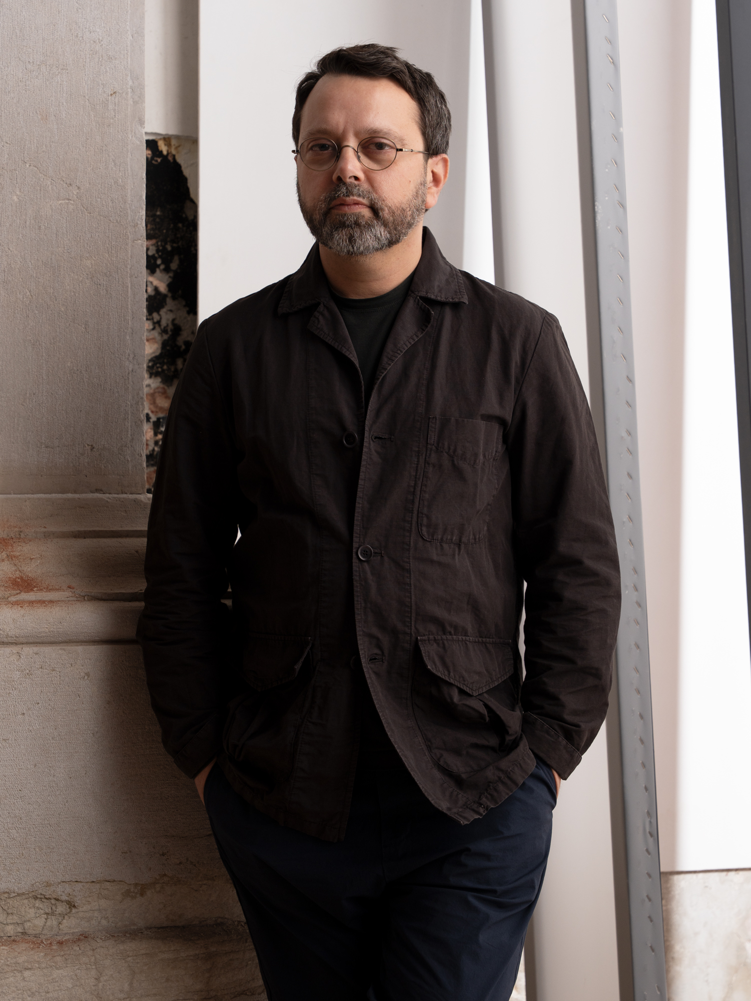 Curator Alessandro Rabottini in all black standing in front of austere exhibition space.