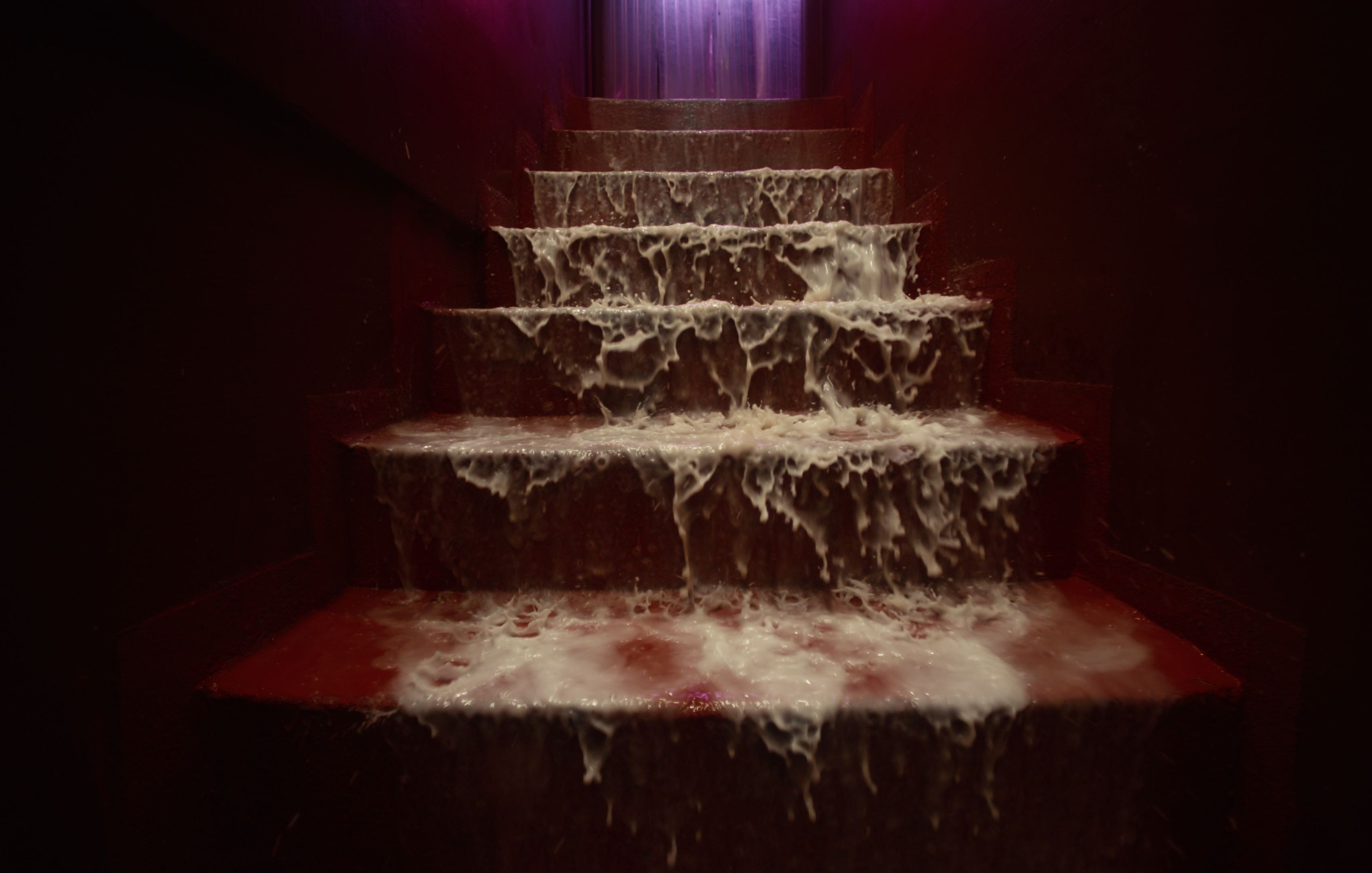 White liquid cascading down dark red staircase under purple light.
