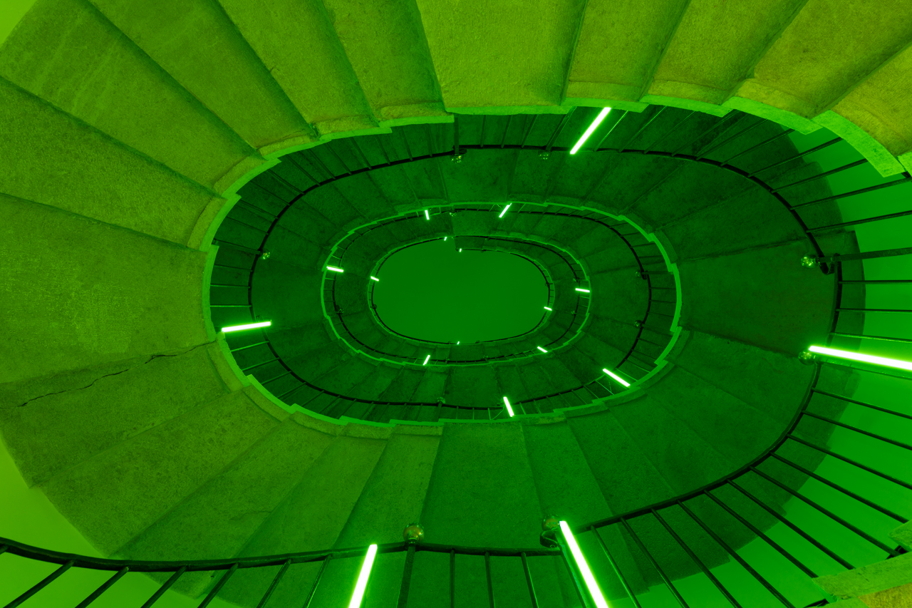Neon green lights spiraling through circular concrete staircase.