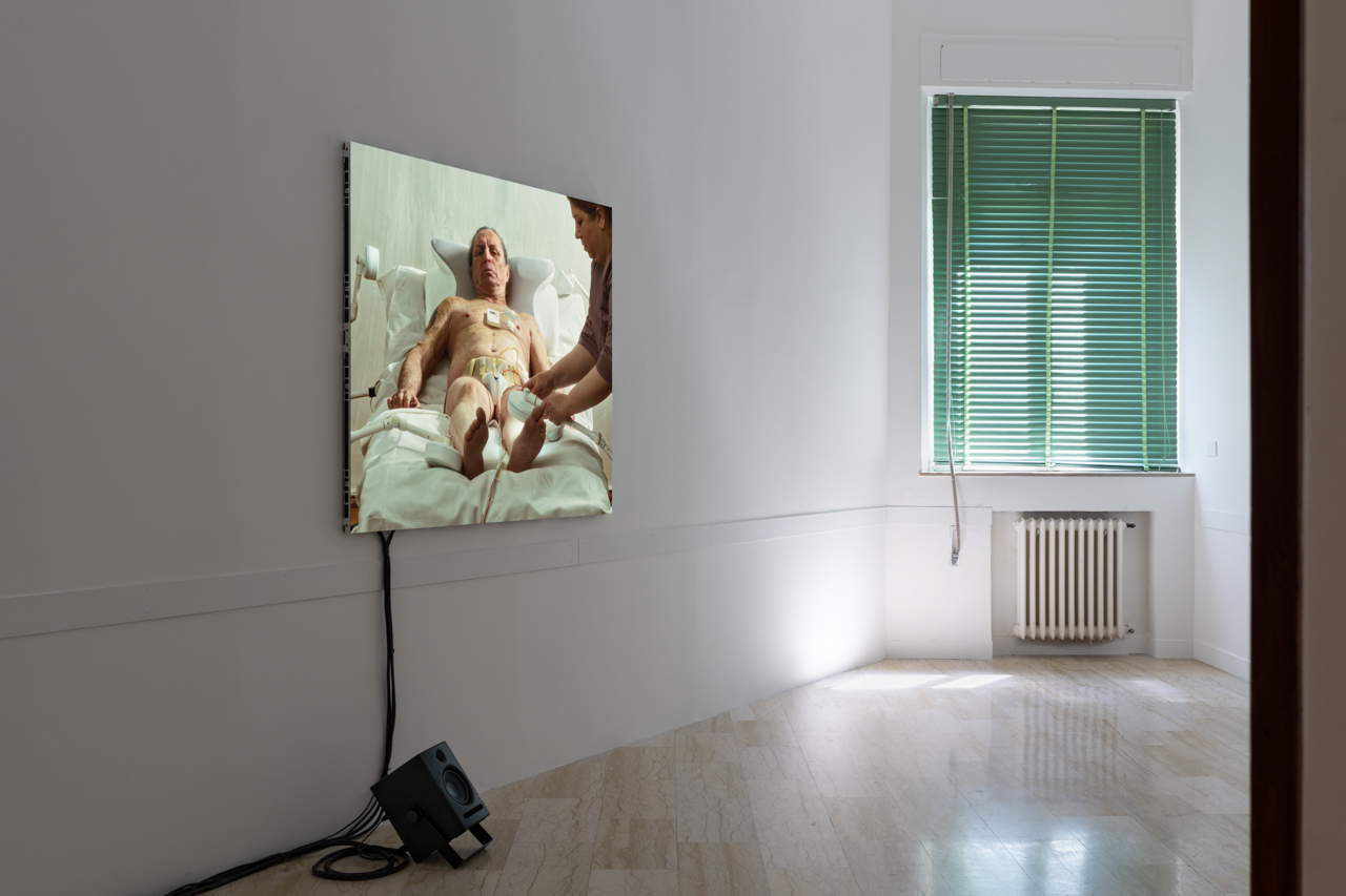 Video screen showing medical procedure in sparse white gallery space.