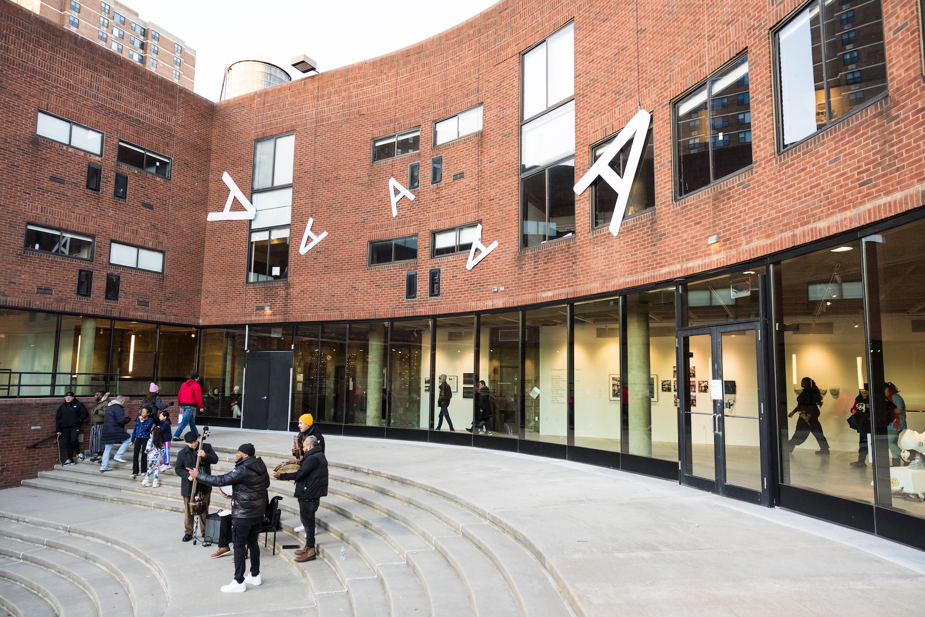 Exterior view of a curved brick arts center courtyard with visitors and musicians.