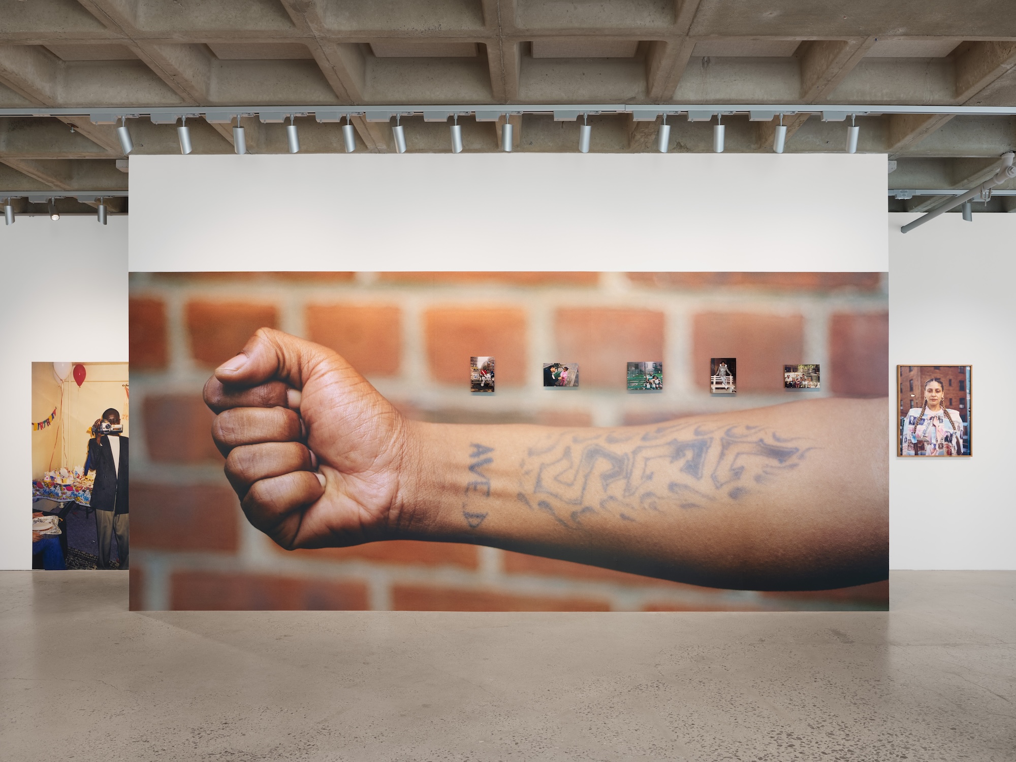 Exhibition view with a large photograph of a tattooed forearm and smaller portraits.