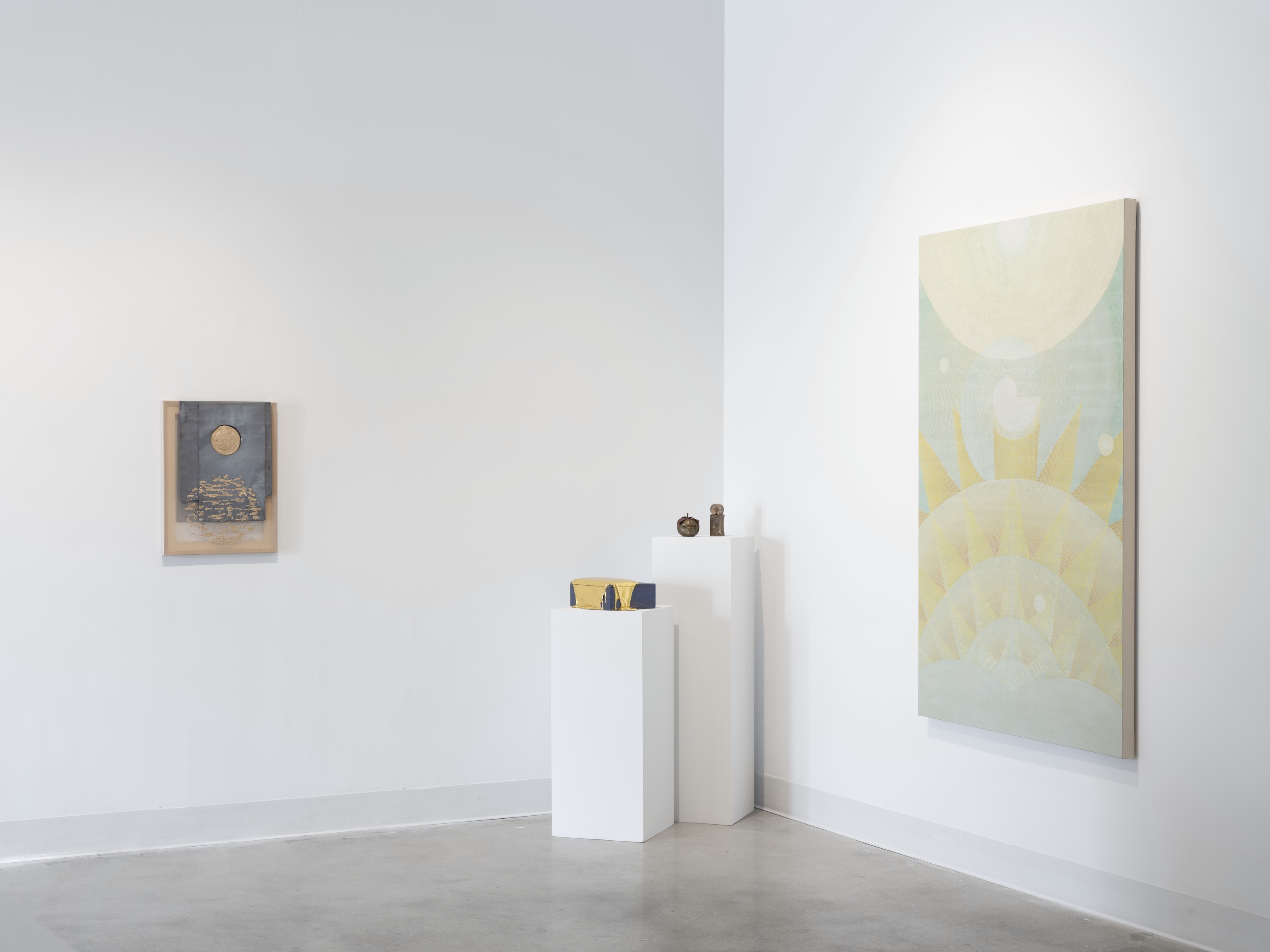Gallery corner installation with two white pedestals holding small sculptures, a large soft-hued painting of stacked circular forms on the right wall, and a mixed-media work on the left wall.
