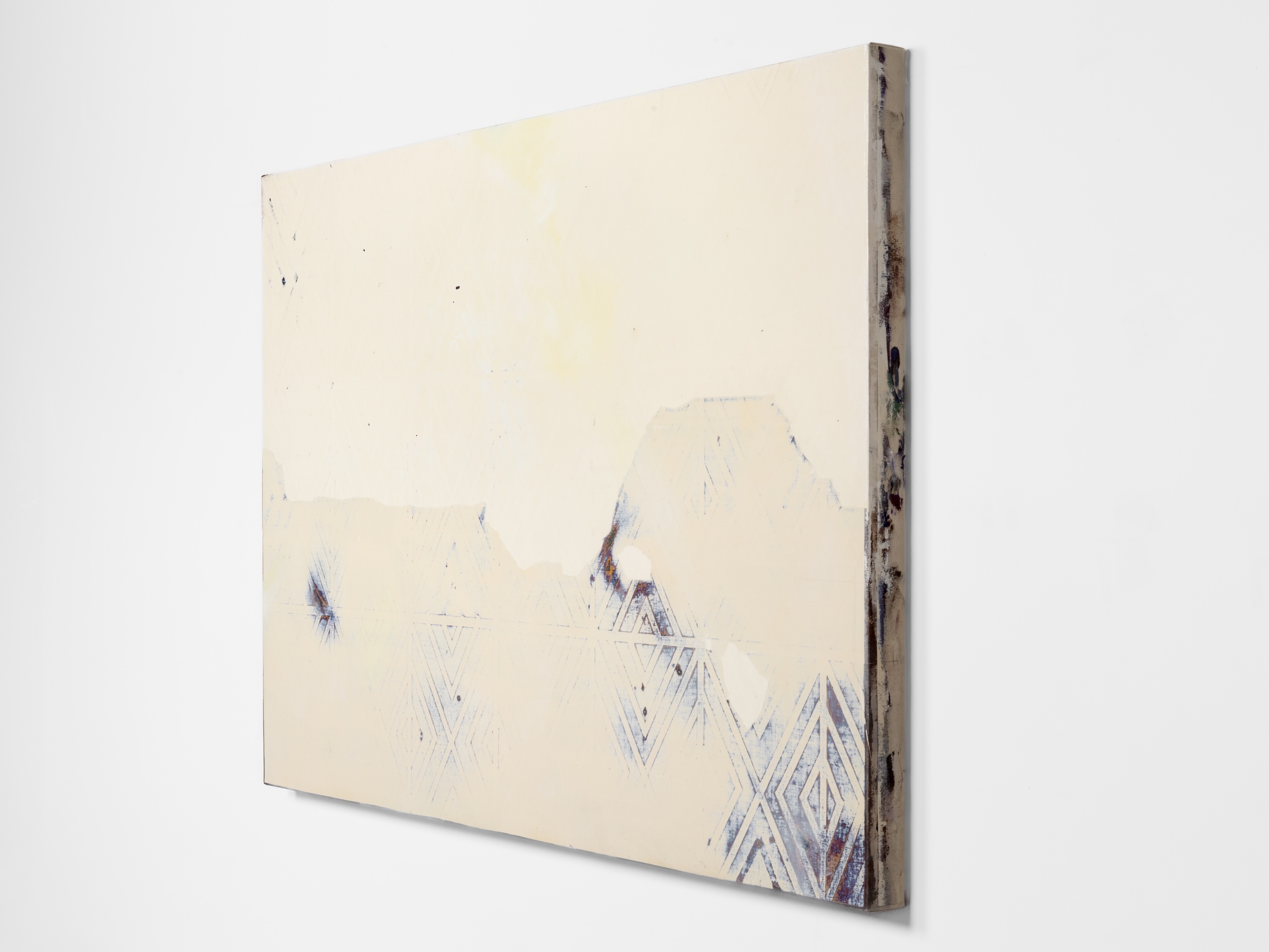 Side-angled view of an abstract painting in pale cream tones with faded triangular and diamond geometric patterns and subtle weathered, mountain-like forms.