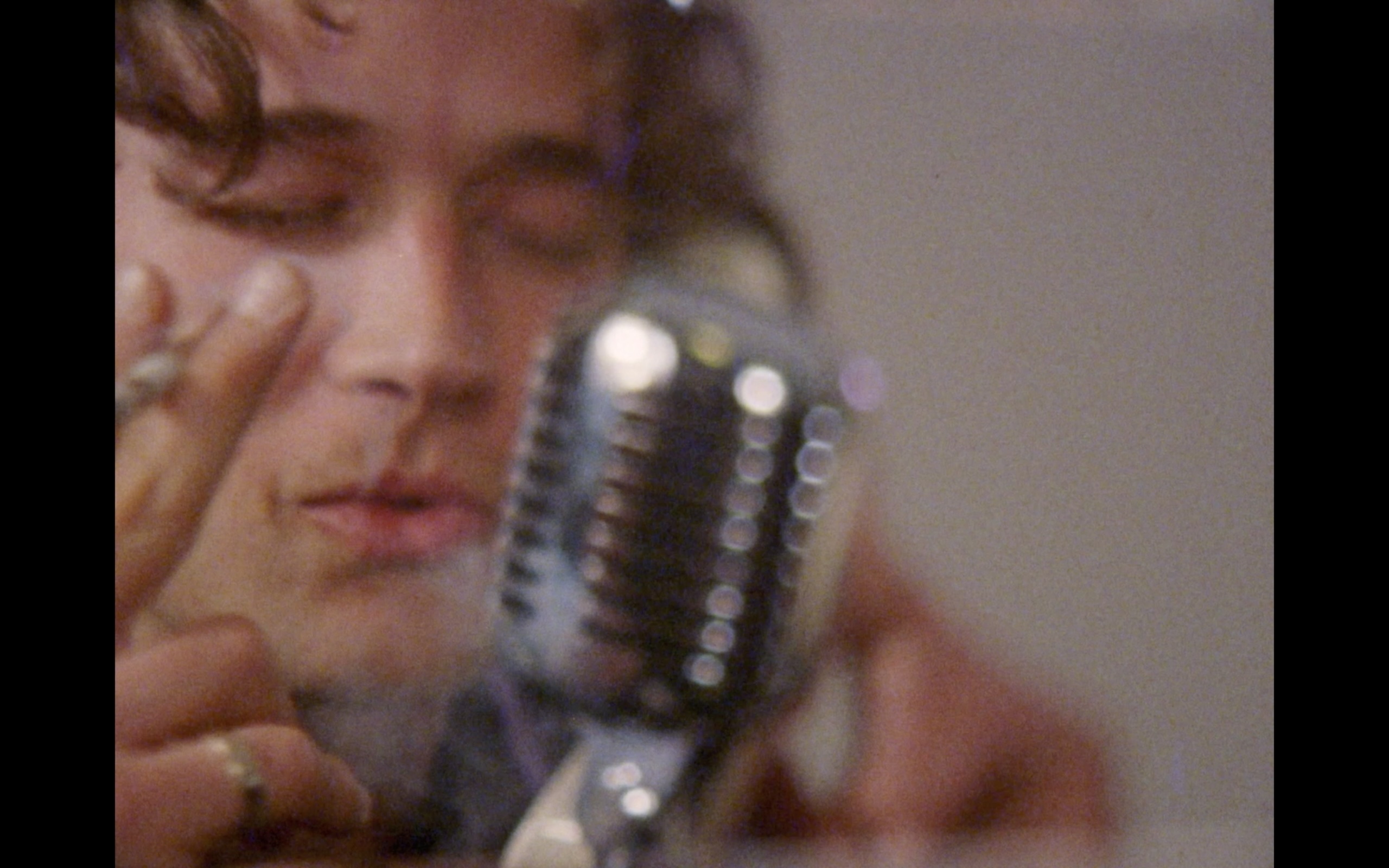 Close-up of a young man's face beside a vintage microphone, eyes closed, hand raised to his temple.