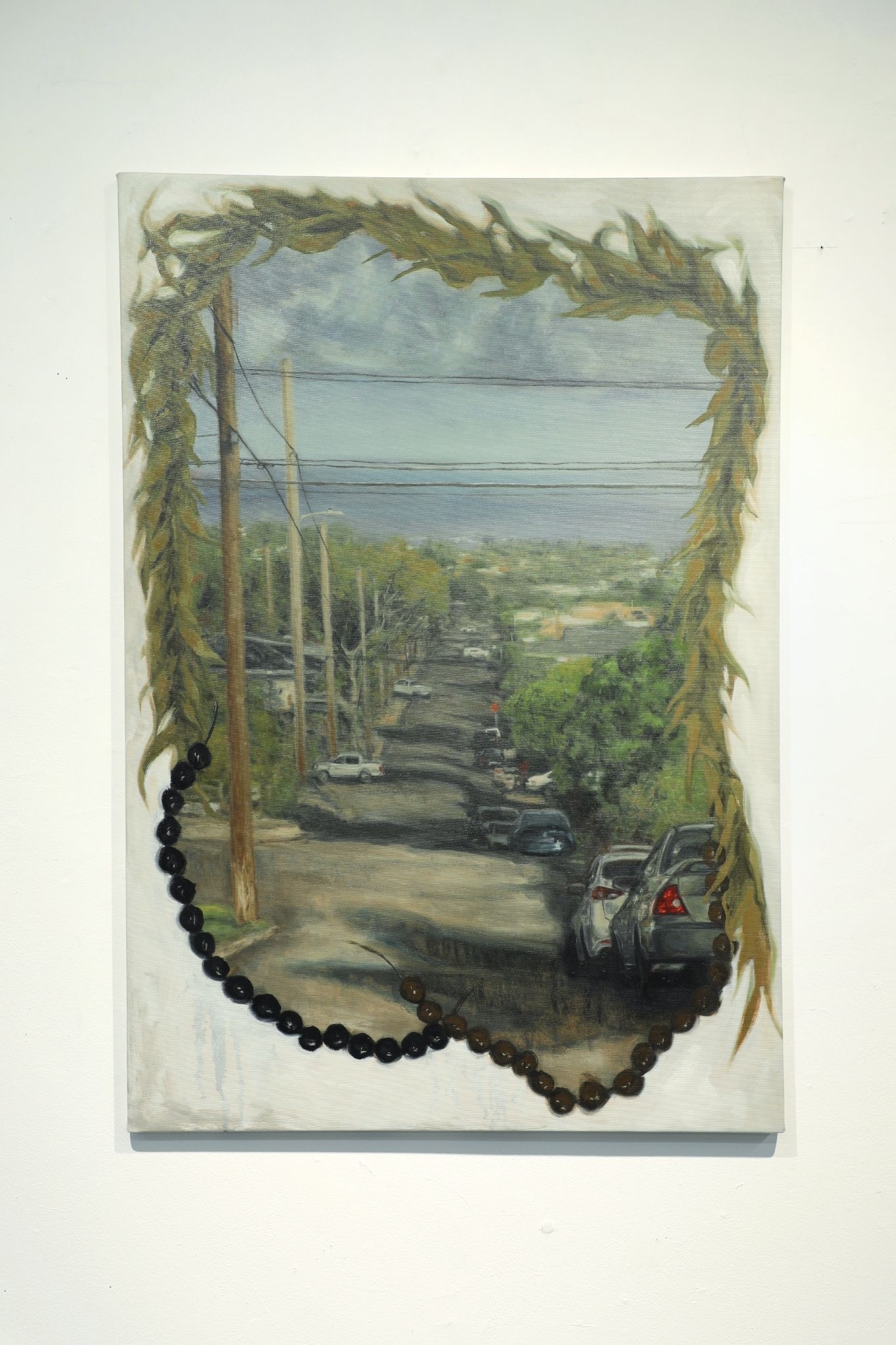 A landscape painting of a residential street overlooking the ocean, framed by painted foliage and embellished with strands of dark beads.