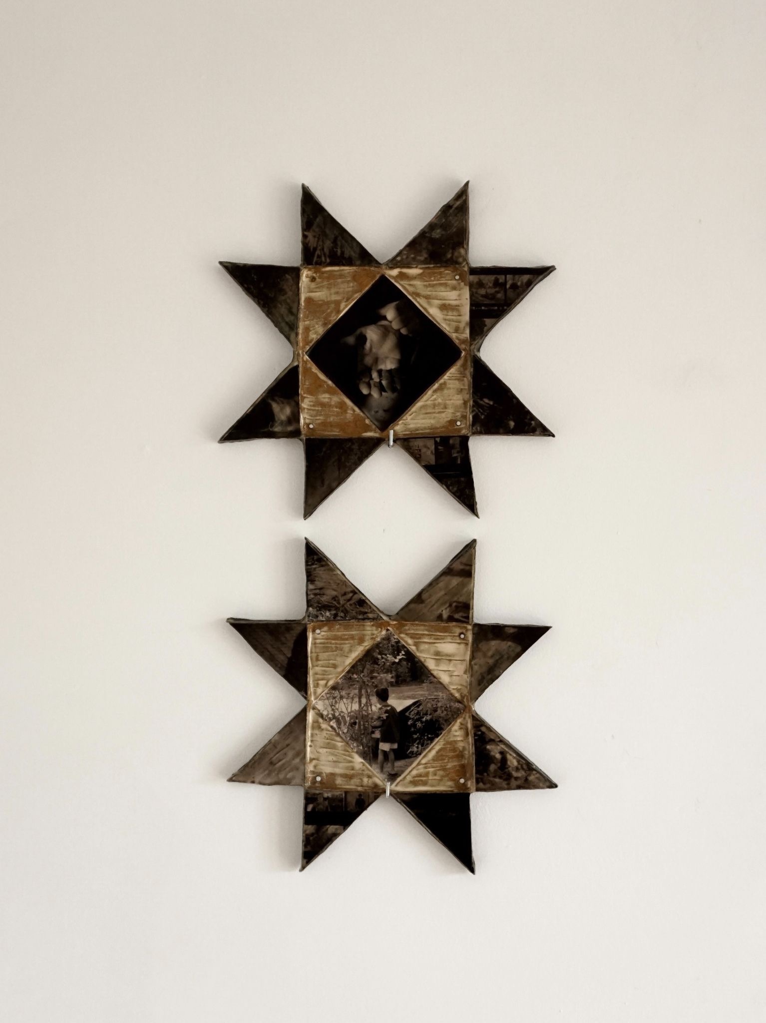 wo star-shaped mixed-media wall sculptures incorporating photographs and weathered wood hang vertically on a white gallery wall.