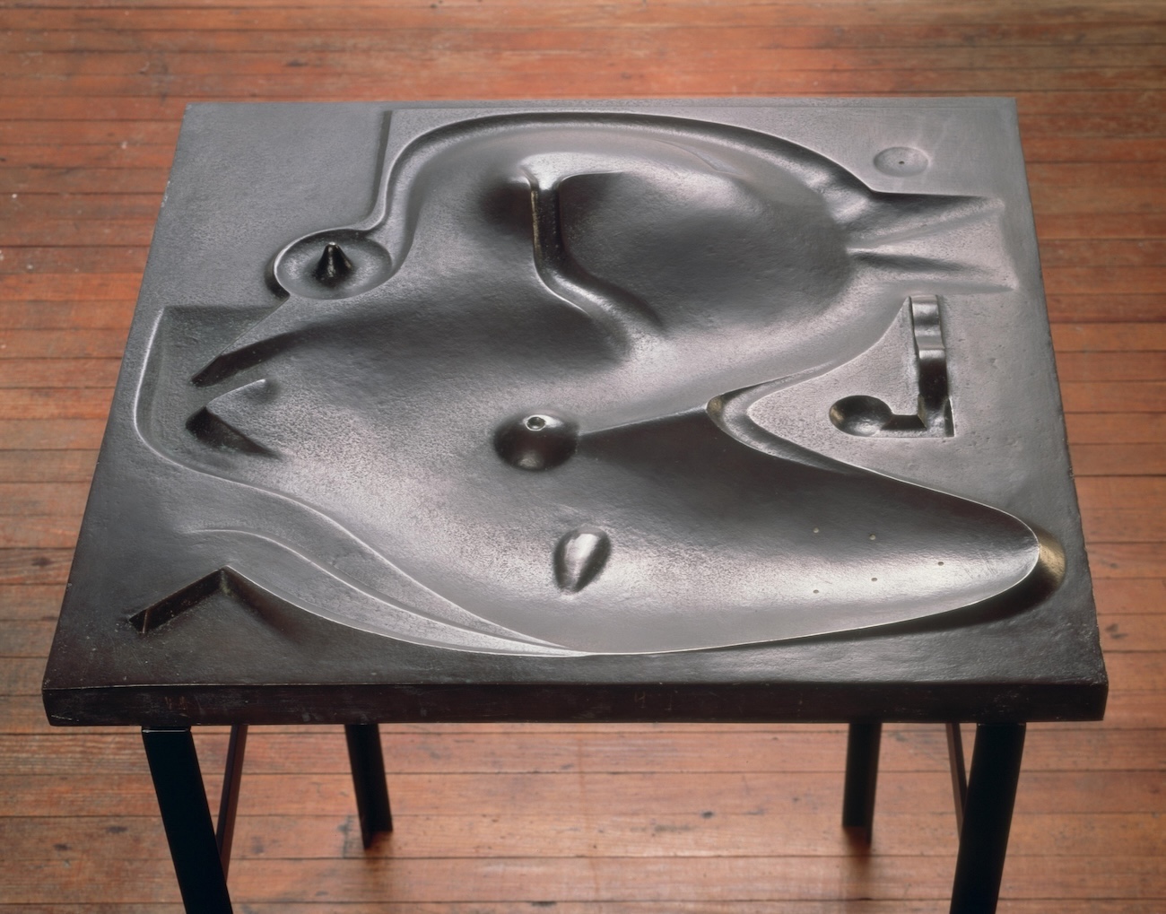 Black bronze table with an abstracted biomorphic relief carved into its surface, suggesting organic curved shapes and hollows, standing on thin metal legs.