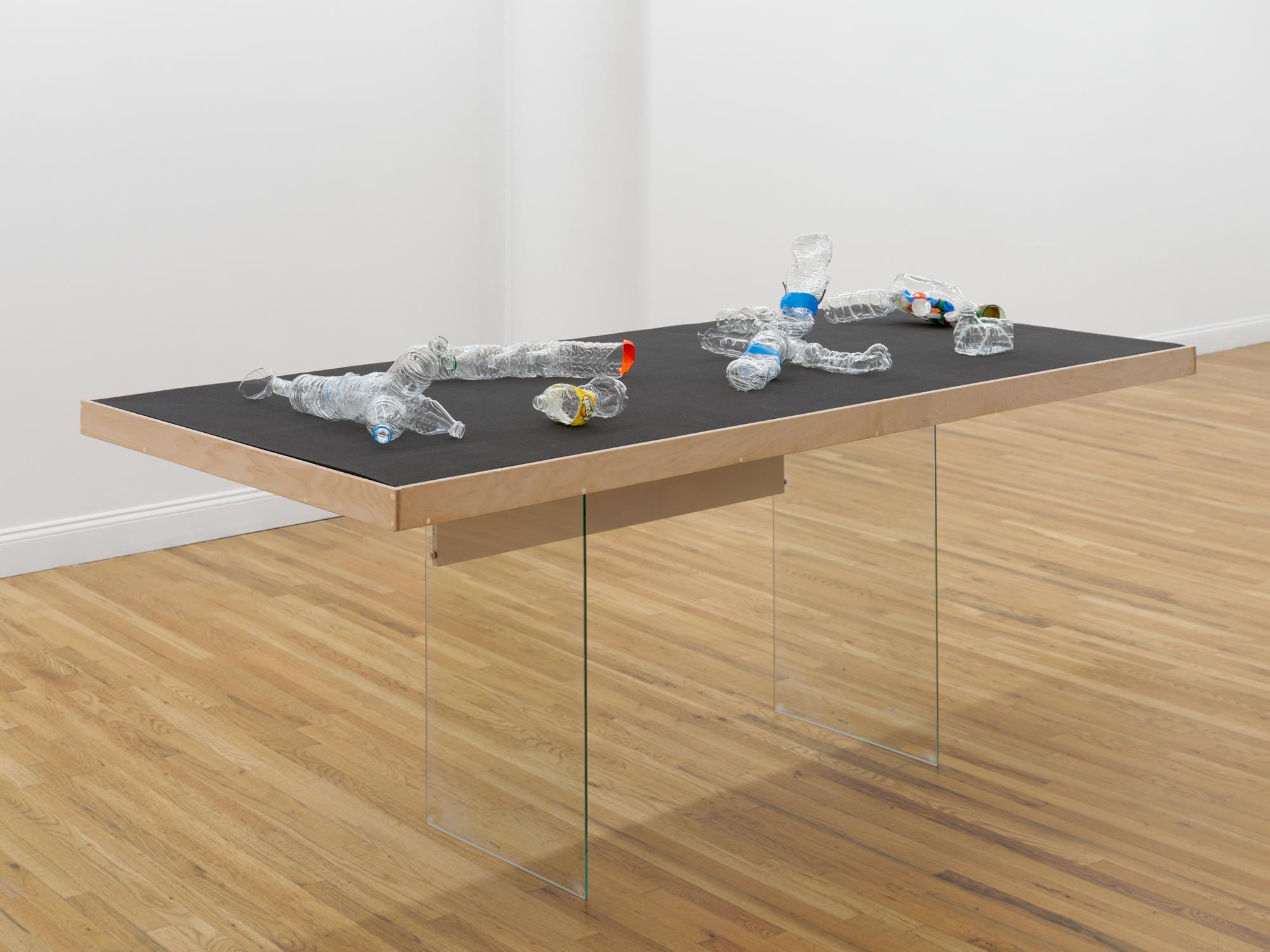 Sculptural forms made from crushed clear plastic bottles arranged across a black tabletop.