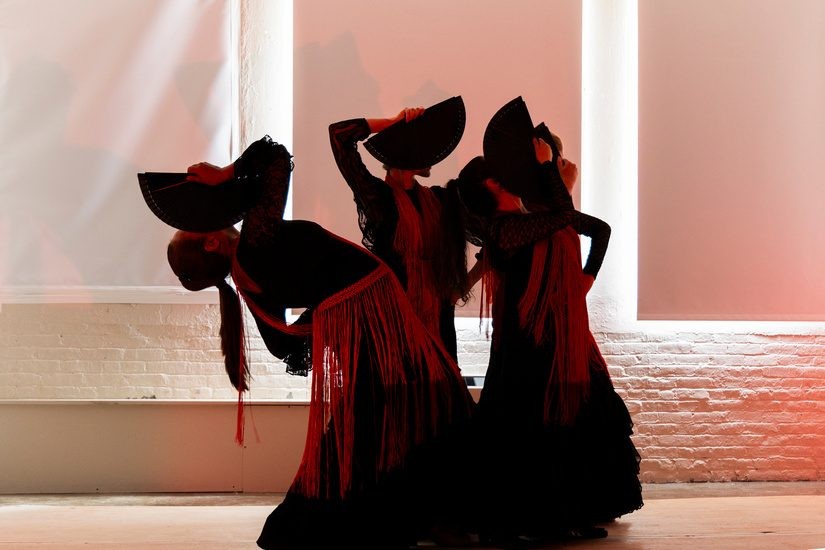 Dancers in long red-and-black costumes bend and raise their arms in silhouette against a bright backdrop.