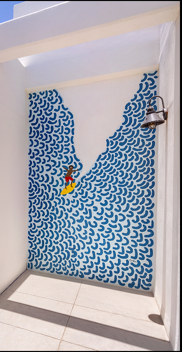 Wall mural of a person surfing a wave made of blue curved brush strokes inside a white-walled corridor with a mounted light fixture.