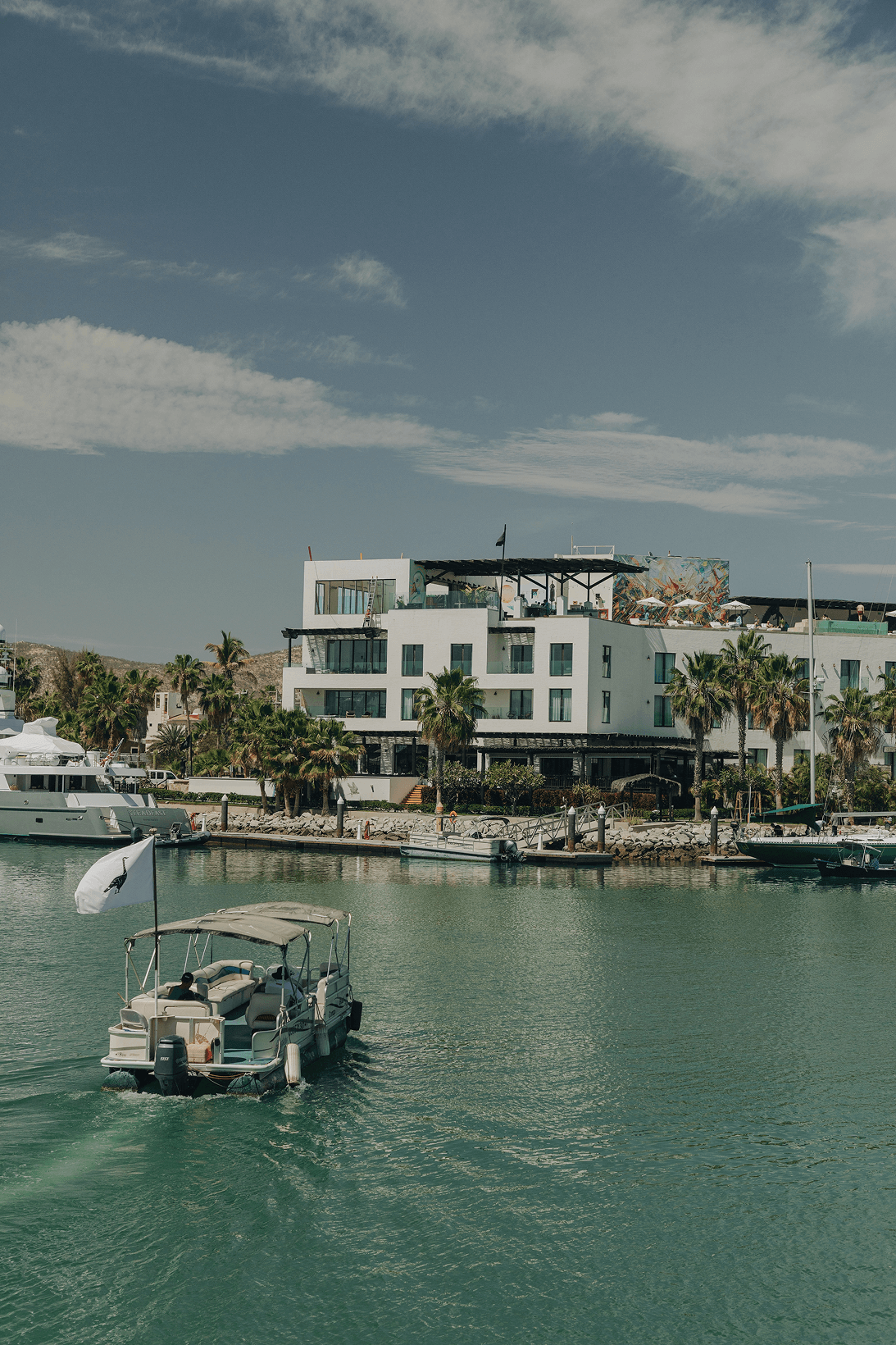 Motorboat with passengers cruising on calm water near a modern white building with palm trees under a partly cloudy sky.