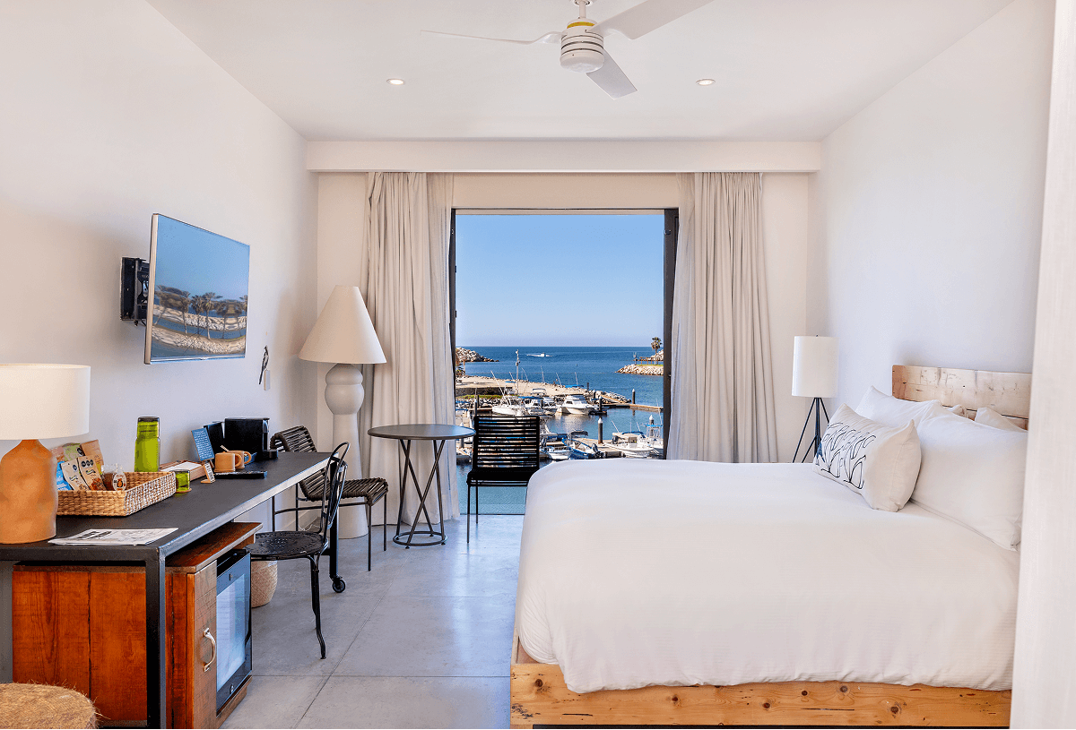Modern hotel room with a king-size bed facing a balcony overlooking a marina and ocean view.