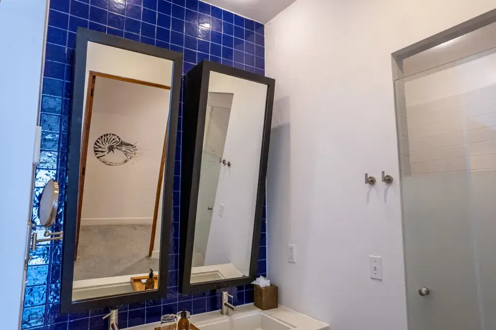 Bathroom vanity with two rectangular mirrors and a sink set against a blue tiled wall and white wall.