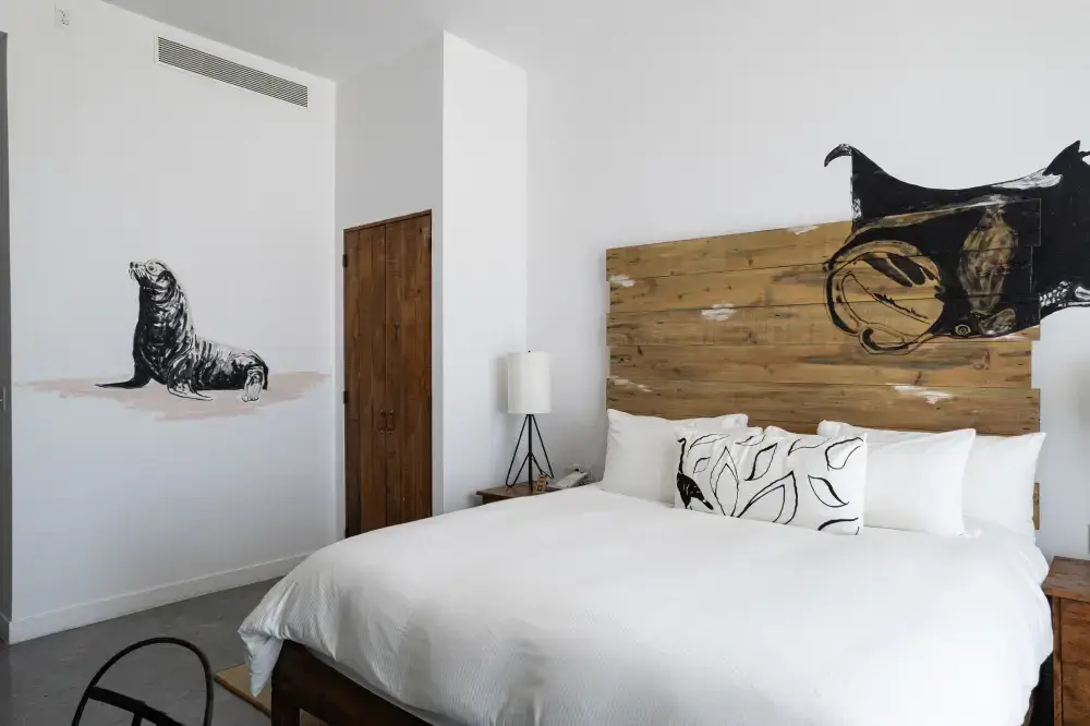 Modern bedroom with a wooden headboard featuring a black and brown animal design, a white bed with patterned pillows, a wooden door, and a seal painted on the wall.