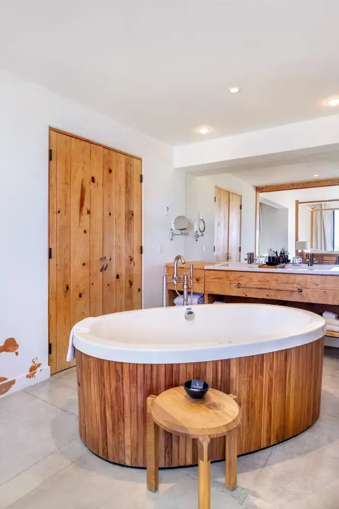 Cuarto de baño moderno con bañera ovalada con marco de madera, tocador de madera con lavabo, espejo grande y puerta de madera.