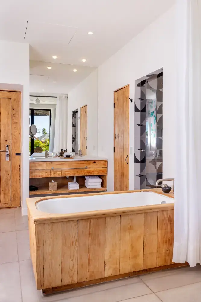 Cuarto de baño moderno con bañera con marco de madera, espejo grande, puertas de madera y toallas debajo del lavabo.