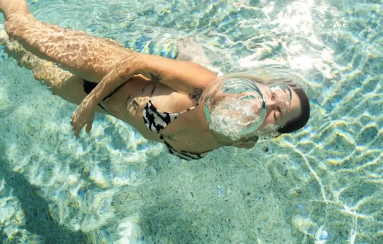 Woman in black and white bikini blowing a large bubble underwater in a clear swimming pool.