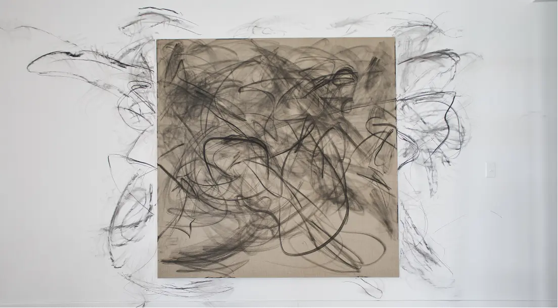 Gran dibujo abstracto al carboncillo con líneas negras onduladas sobre un lienzo beige, que se extiende hasta la pared blanca circundante.