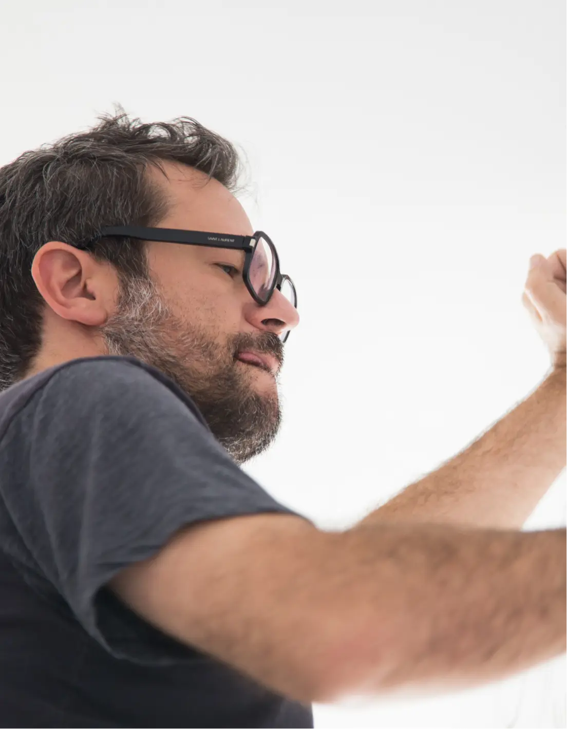 Man with glasses and beard wearing a dark t-shirt against a white background.