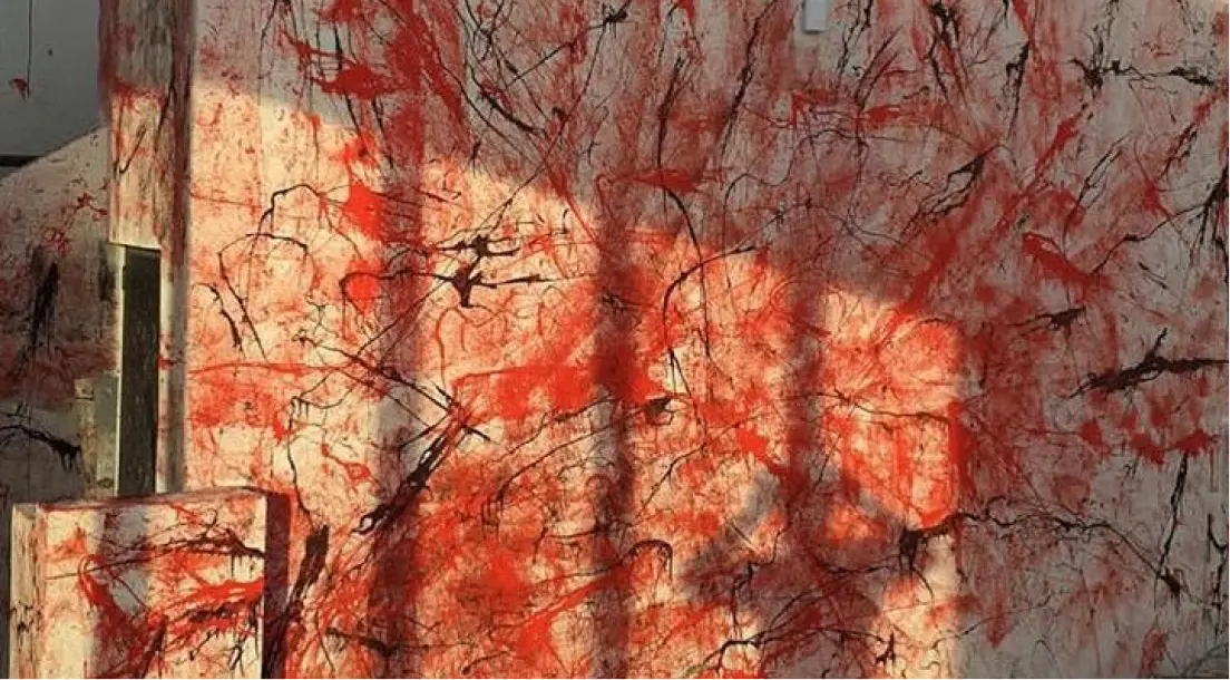 Pared cubierta con salpicaduras y rayas abstractas de pintura roja y negra, con sombras proyectadas sobre ella.