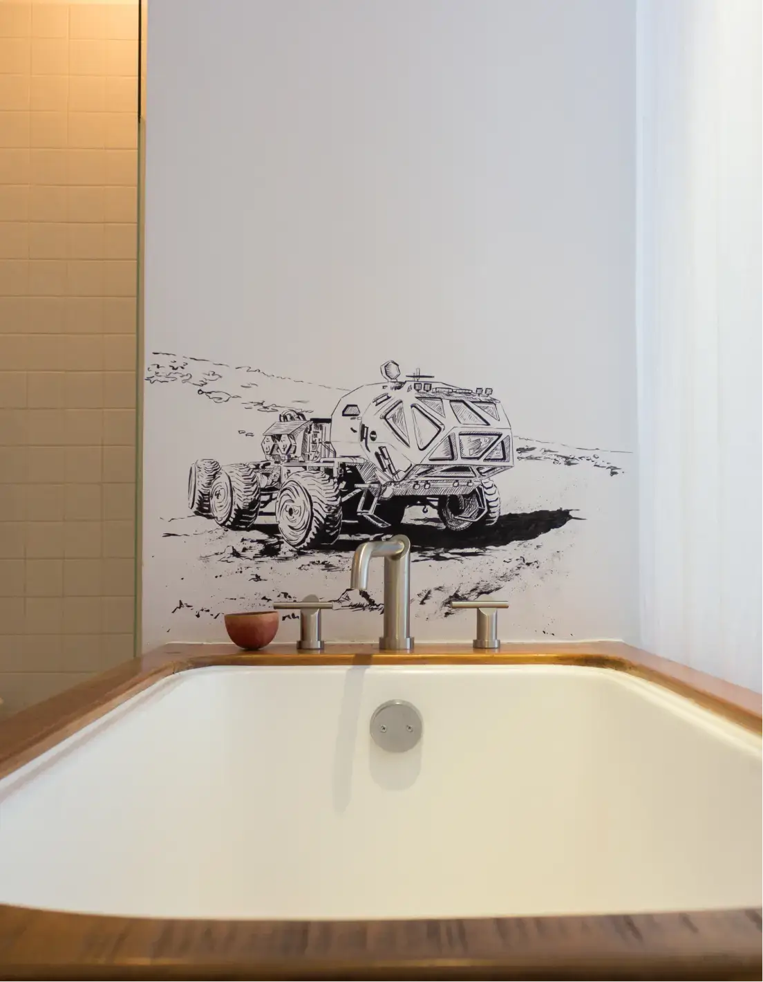 Bañera blanca con bordes de madera y grifo moderno frente a una pared con un dibujo en blanco y negro de un vehículo explorador futurista sobre terreno rocoso.