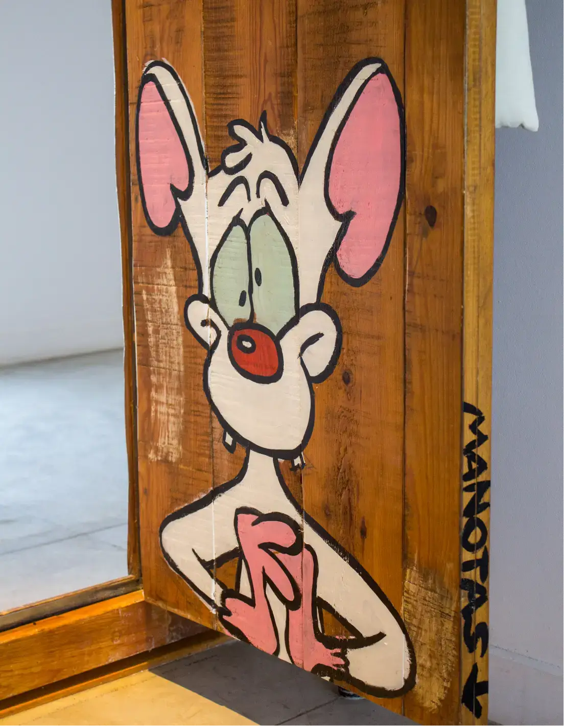 Pintura de un ratón de dibujos animados con grandes orejas rosas y una nariz roja sobre paneles de madera.