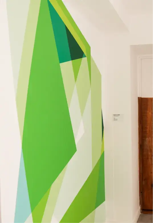 Abstract geometric wall mural with overlapping green, yellow, and blue shapes in a modern interior.