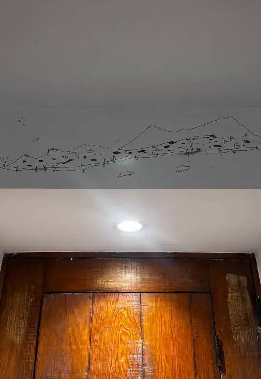 Wooden door with a glowing recessed ceiling light above and a simple black line drawing of mountains, trees, and a sun on the wall above the door.