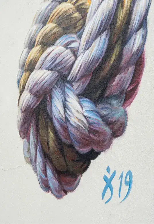 Close-up of a wall mural depicting a thick, multi-colored rope tied in a knot with the artist's signature and date '19' in blue.