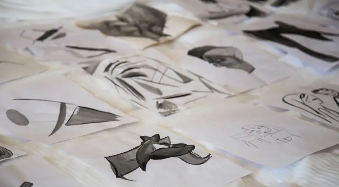 Close-up of various black ink sketches on white paper sheets spread out on a flat surface.