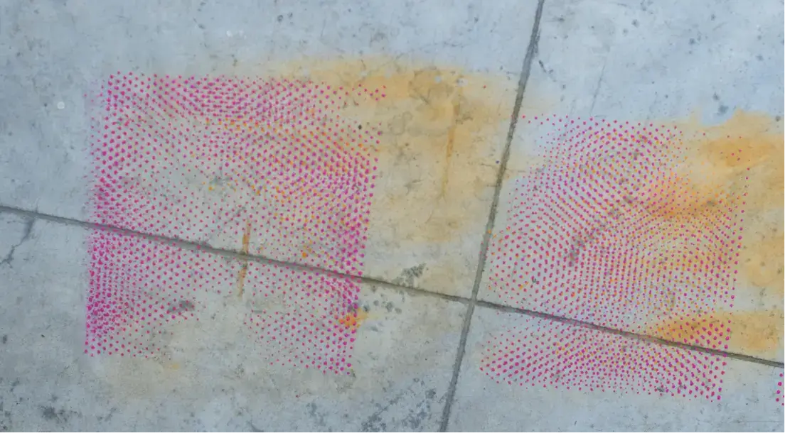 Concrete floor with intersecting cracks and faded yellow stains, featuring two adjacent pink dotted square patterns.