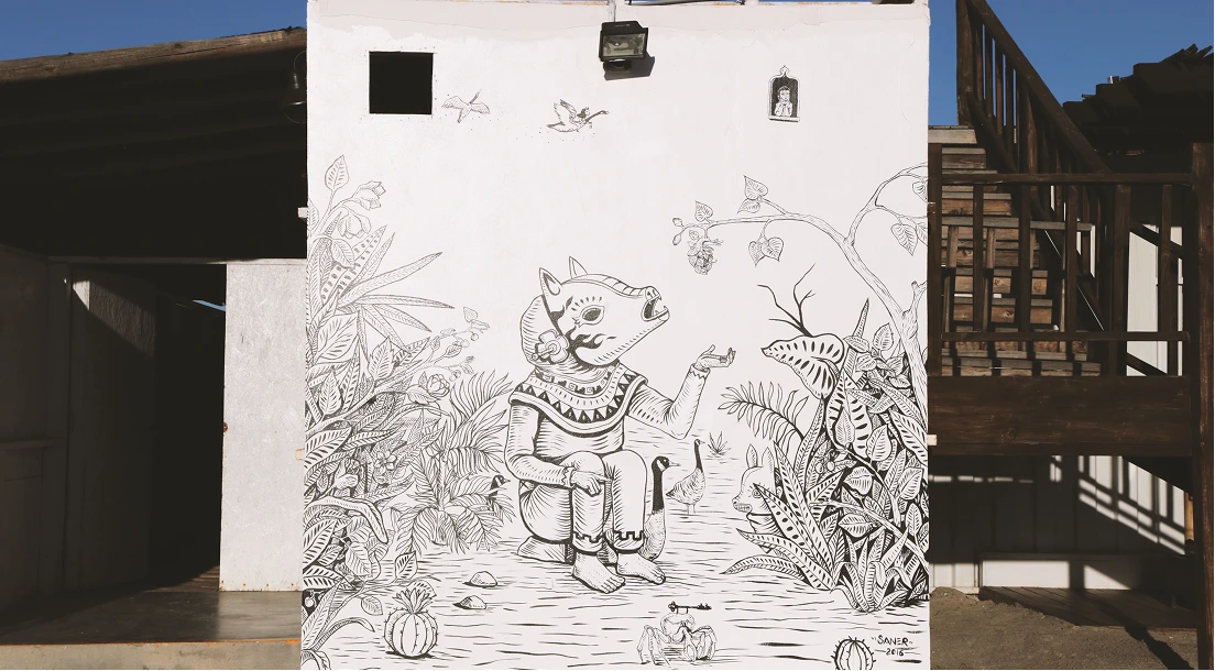 Black and white mural painting on a white wall depicting a seated figure with an animal head surrounded by plants, birds, and animals.