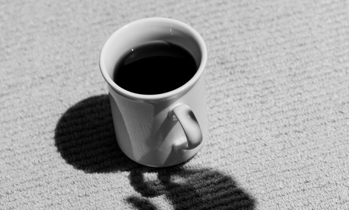 Taza de cerámica blanca llena de café negro proyectando una sombra sobre una superficie texturizada.