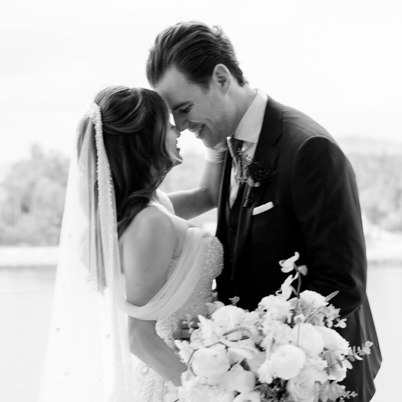 Bride and groom smiling and embracing closely on their wedding day, bride holding a large bouquet.