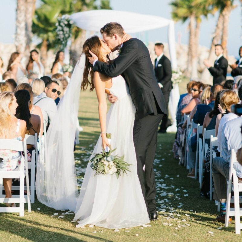 Bride and groom sharing a kiss at an outdoor wedding ceremony with seated guests watching.