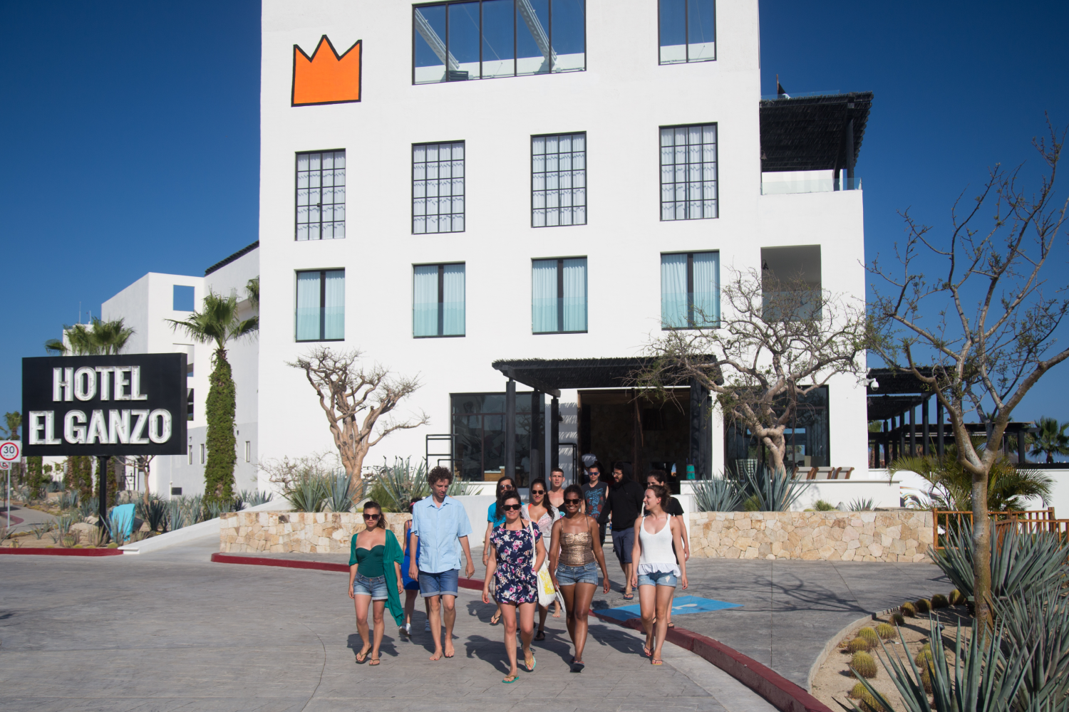 Group of people walking barefoot outside the Hotel El Ganzo under clear blue sky.