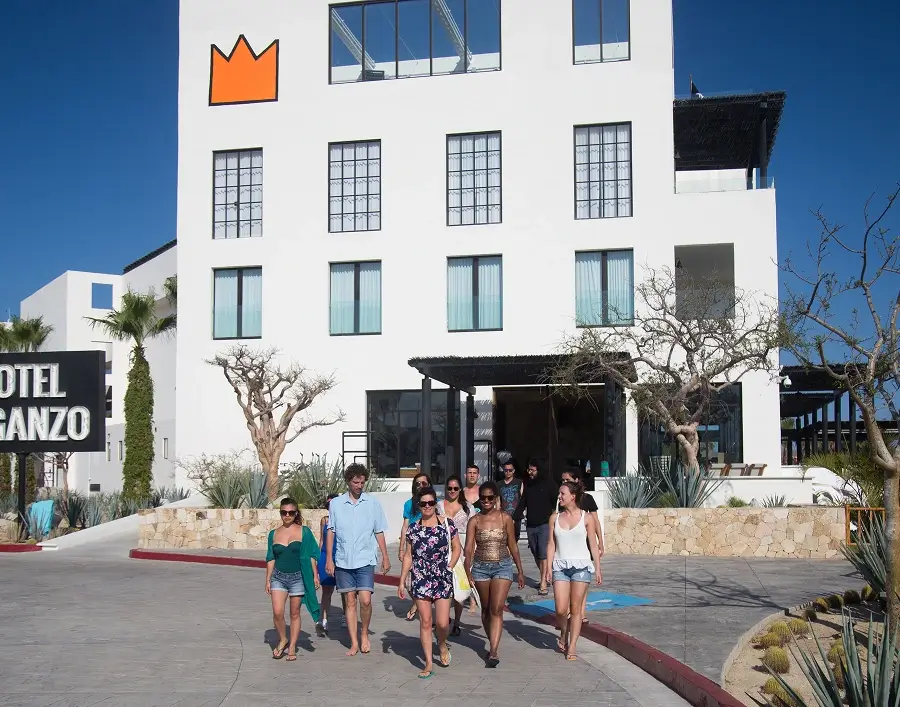 Grupo de personas caminando descalzas frente al Hotel El Ganzo bajo un cielo azul claro.