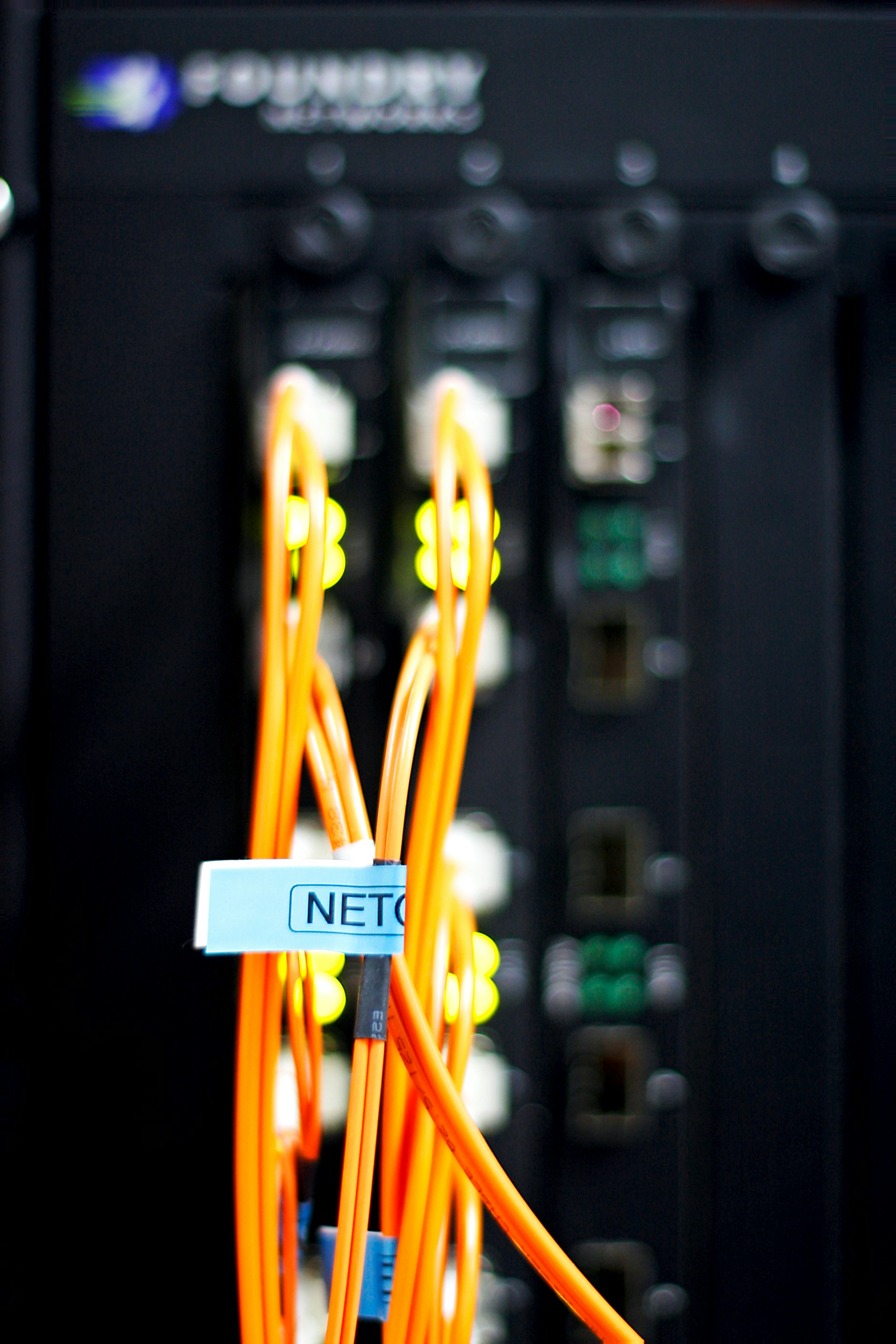 Close-up of orange network cables connected to a black networking device with LED indicator lights.