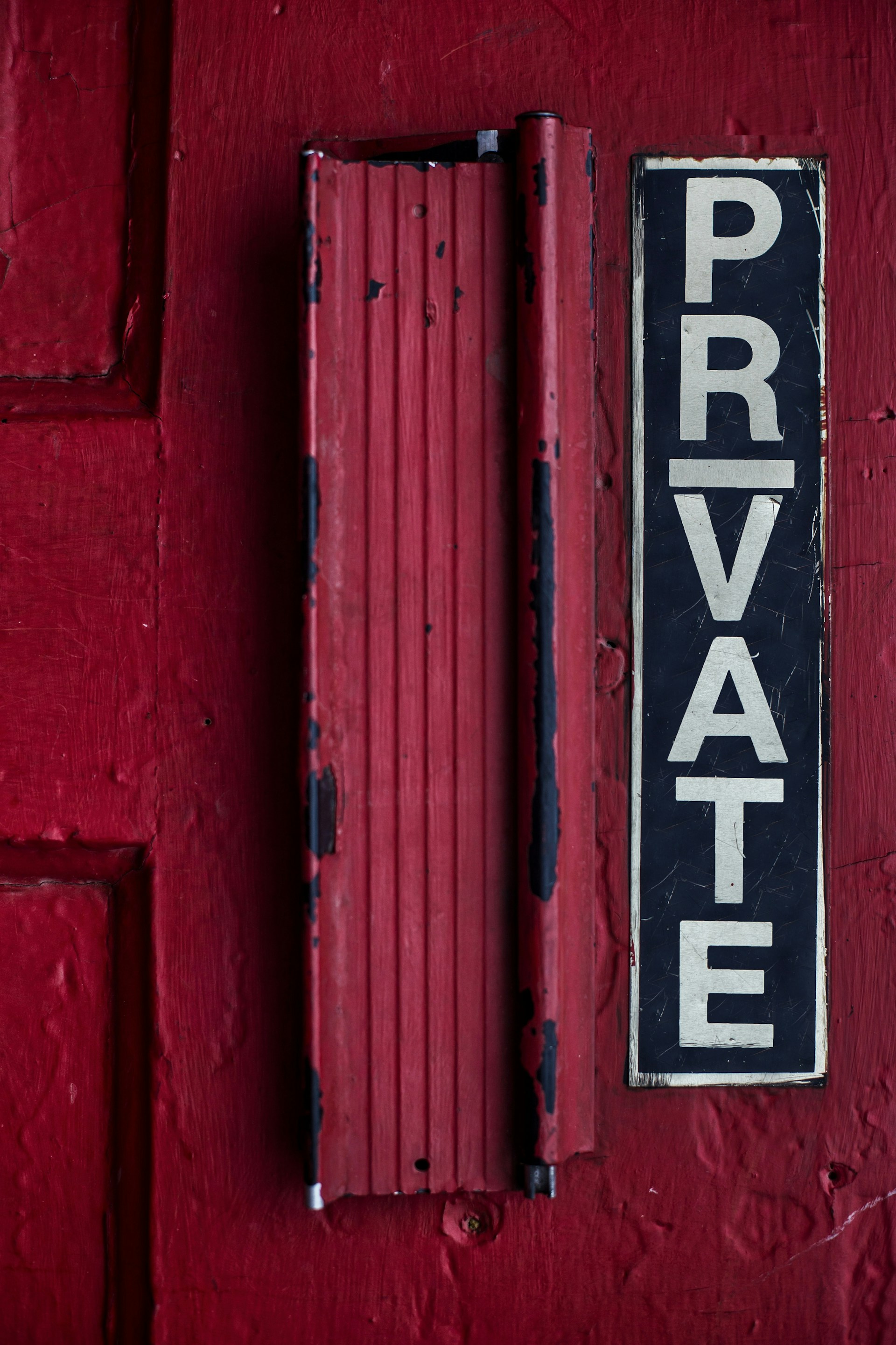 Close-up of a weathered red door with a vertical black and white sign reading 'PRIVATE'.