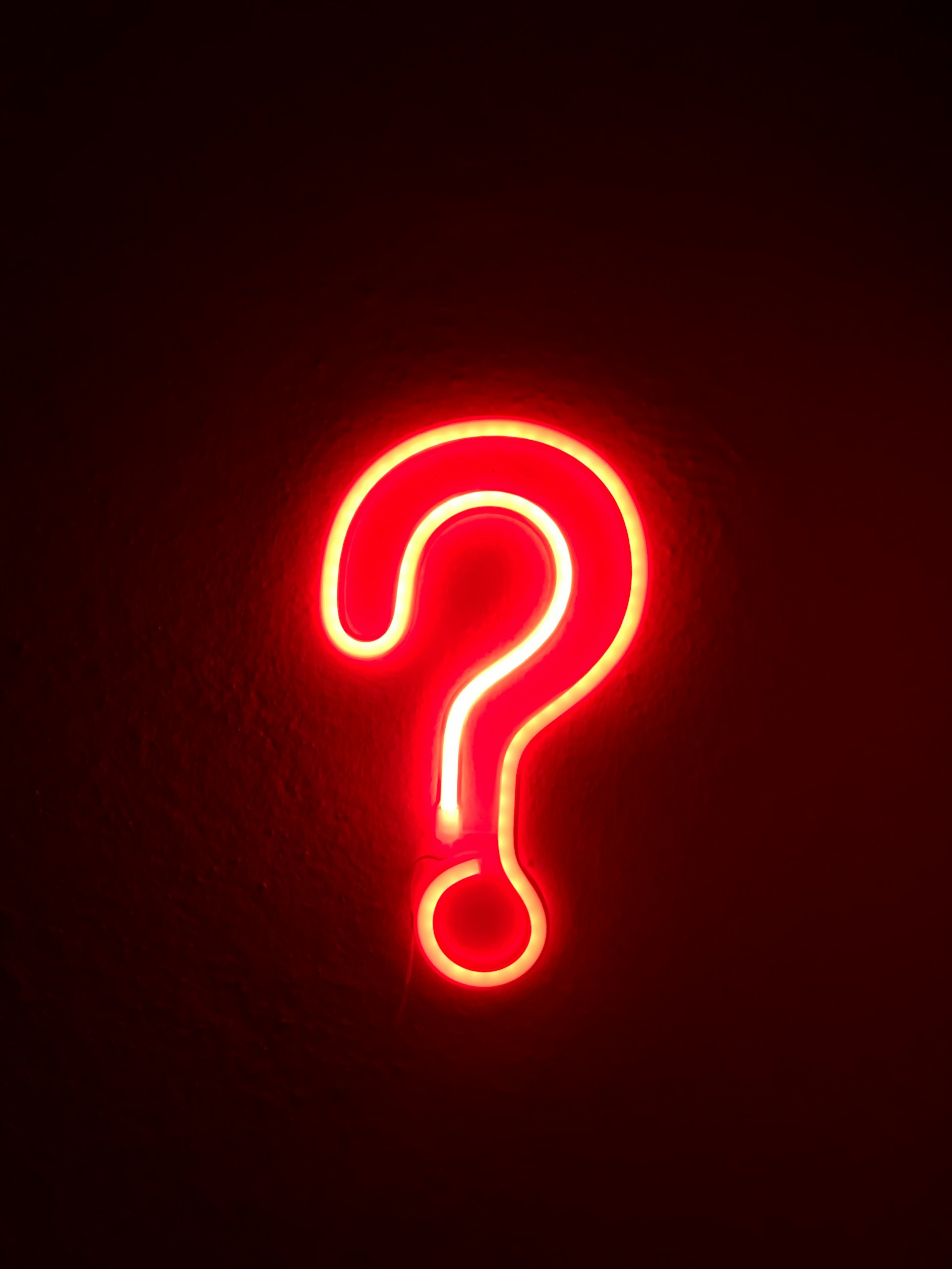 Red neon light shaped like a question mark on a dark wall.