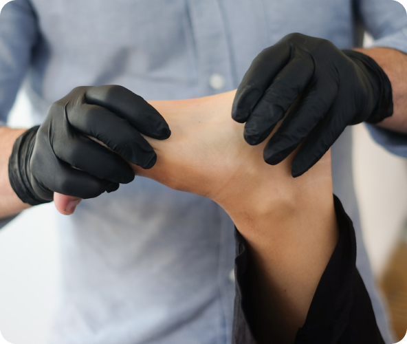 Person wearing black gloves holding and stretching another person's ankle.