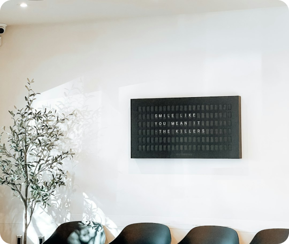 Modern interior with a potted olive tree, black chairs, and a black letter board on the wall reading 'SMILE LIKE YOU MEAN IT THE KILLERS'.