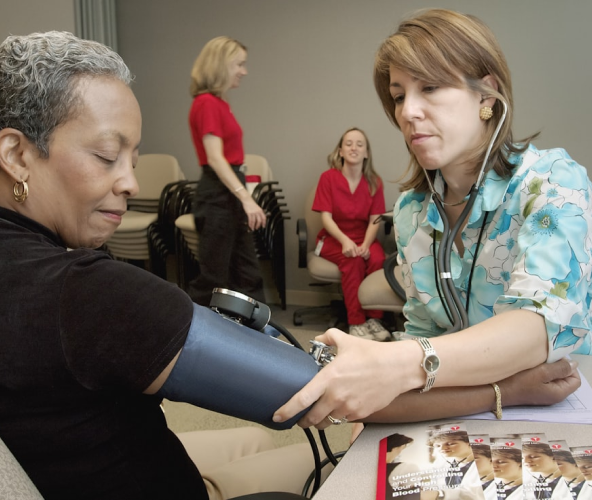 Healthcare professional measuring blood pressure of a seated older woman using a sphygmomanometer in a clinic setting.