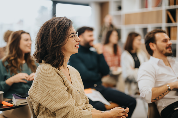 Diverse group of adults attentively listening in a classroom or workshop setting.