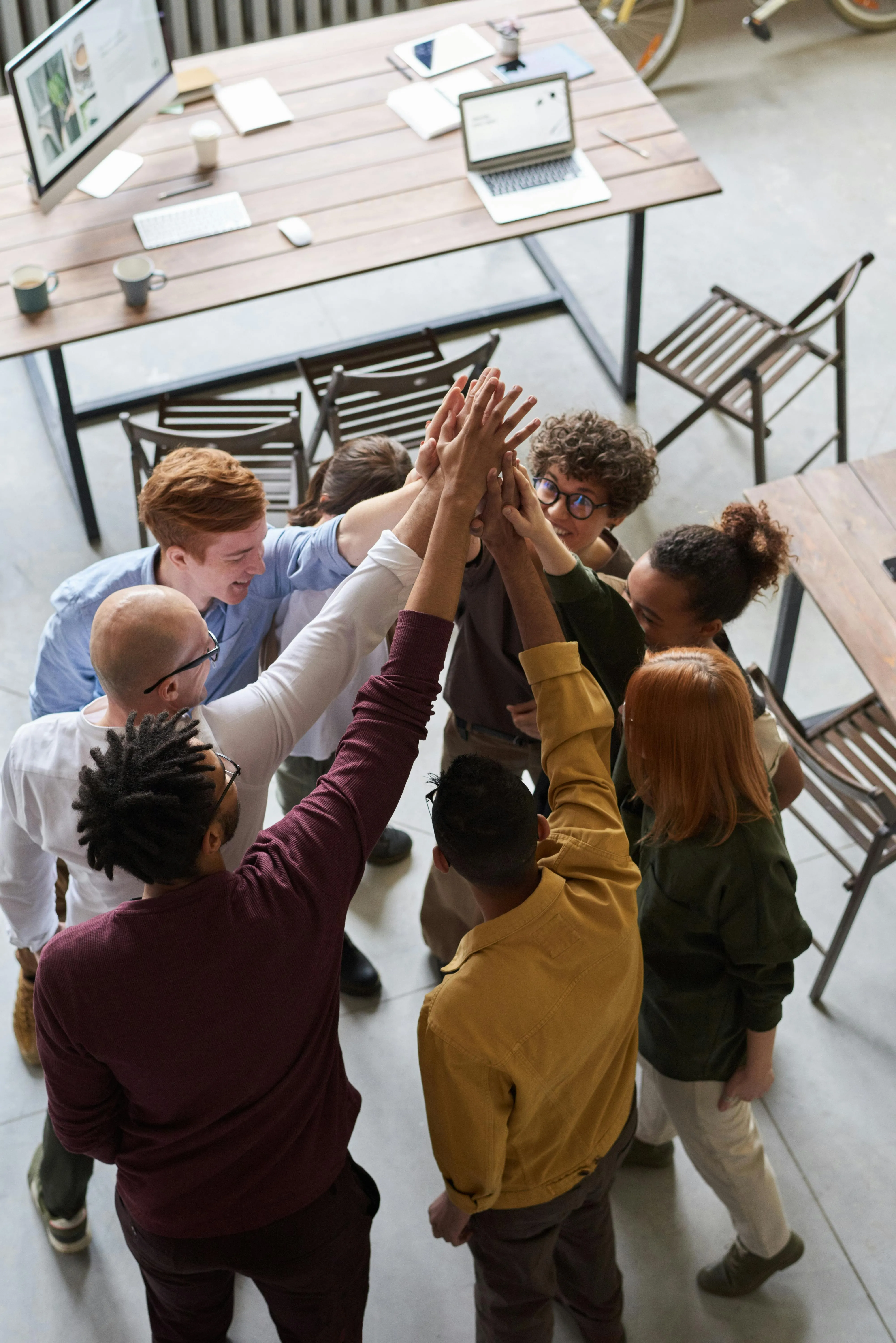 An aerial view photograph of a diverse group of professionals huddled in a circle with their hands stacked in the center, representing collaboration and shared company values in a modern office.