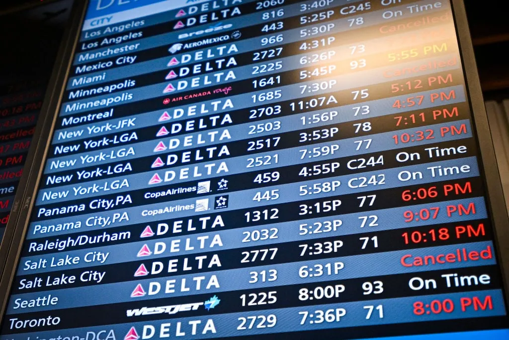 A close-up of an electronic airport departures board displaying real-time flight information, including destinations, airline logos like Delta and Copa Airlines, flight numbers, and updated statuses such as 'On Time' or 'Cancelled'.