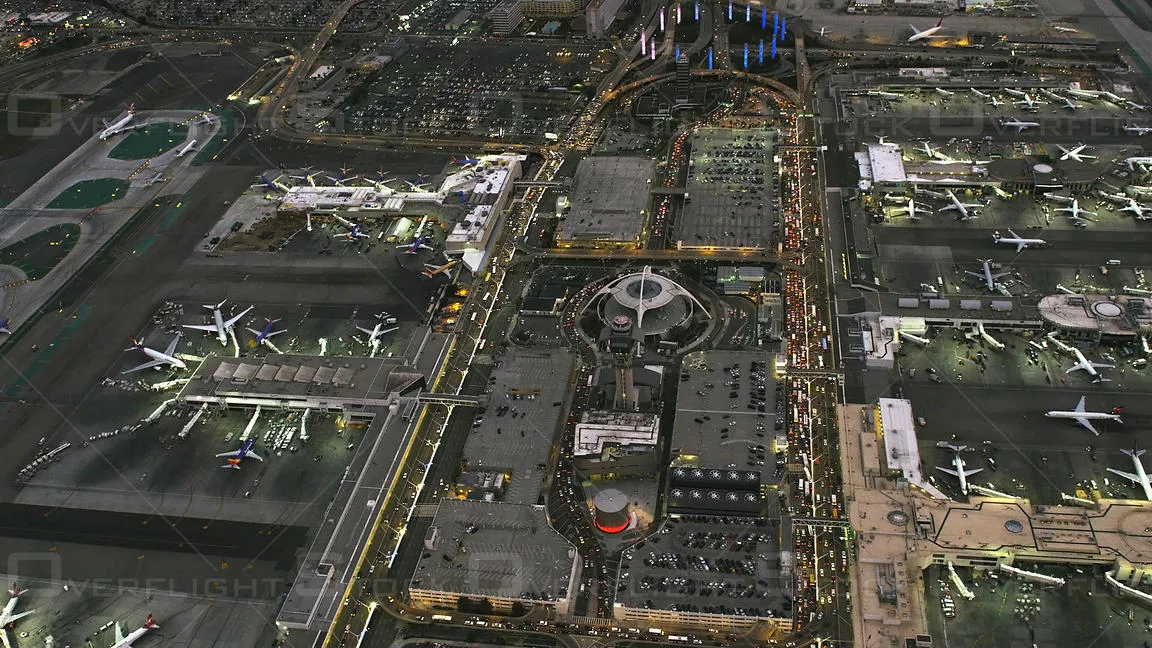A comprehensive aerial view of Los Angeles International Airport (LAX) at night, showcasing terminal layouts, the Theme Building, parked commercial aircraft, and the dense traffic flow of the horseshoe loop.